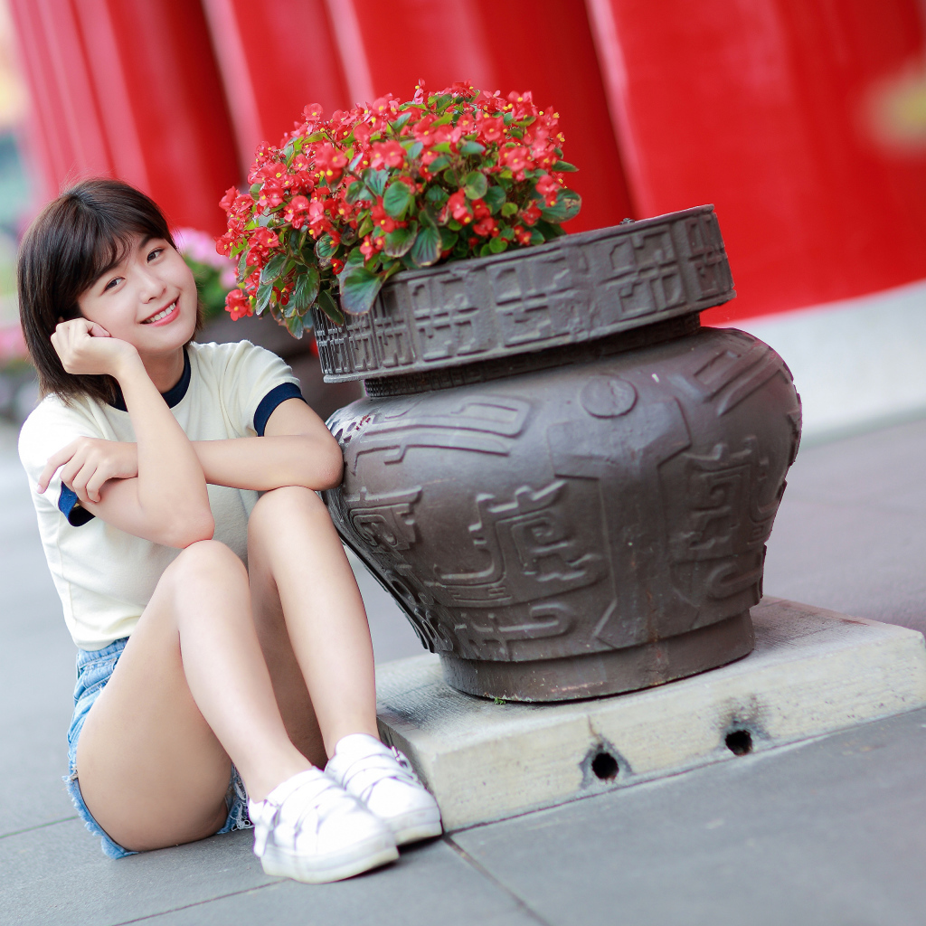 Улыбающаяся азиатка сидит у клумбы с цветами