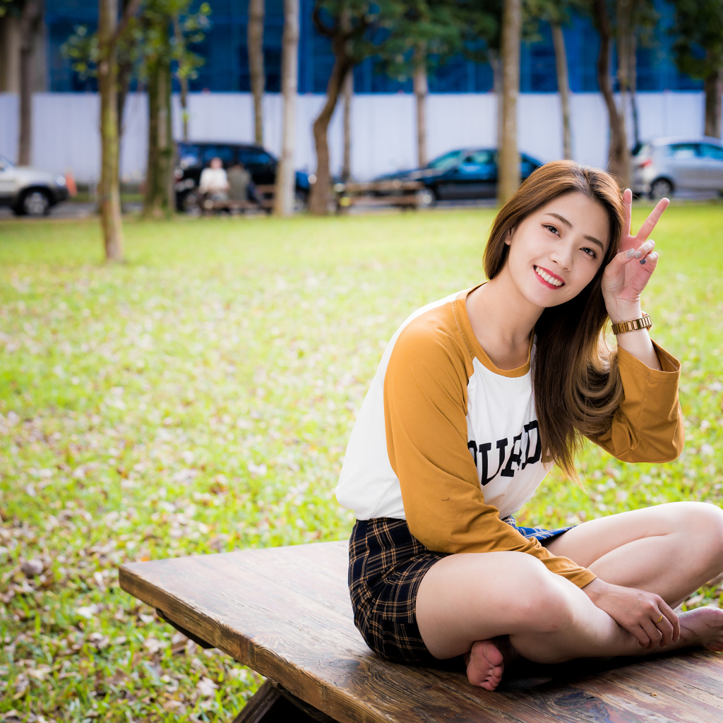 Улыбающаяся девушка азиатка сидит на лавке в парке 