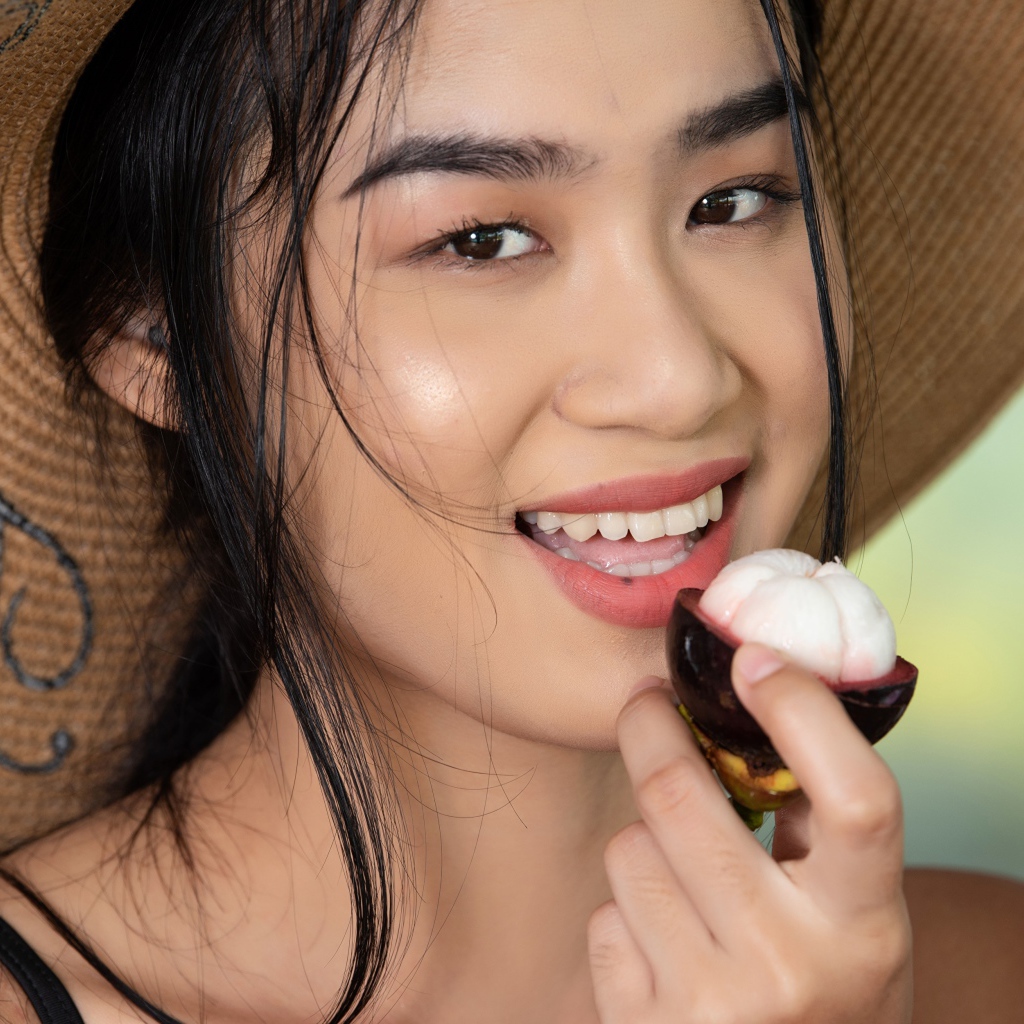 Улыбающаяся азиатка в шляпе с фруктом в руке