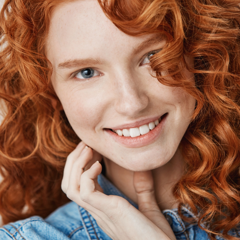 Улыбающаяся голубоглазая рыжеволосая девушка в джинсовой куртке 