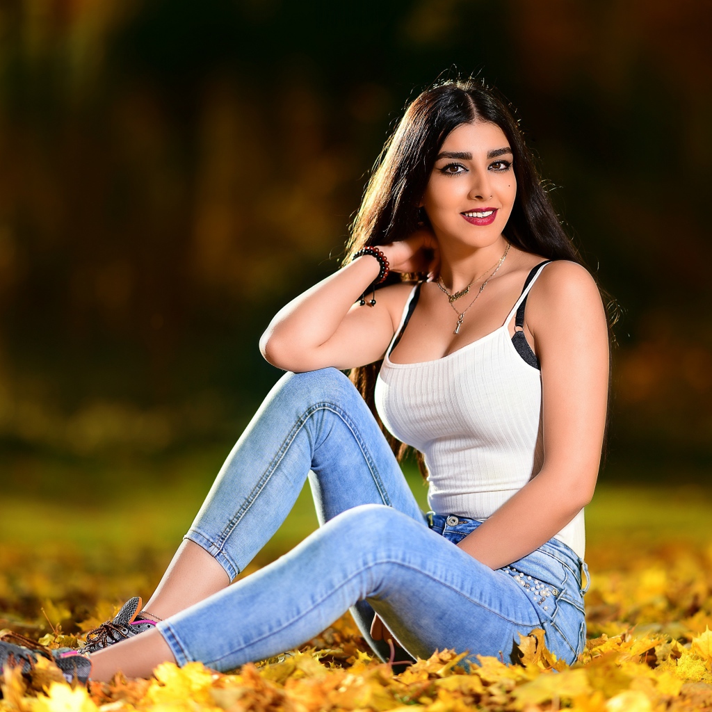 Улыбающаяся брюнетка сидит на опавшей листве