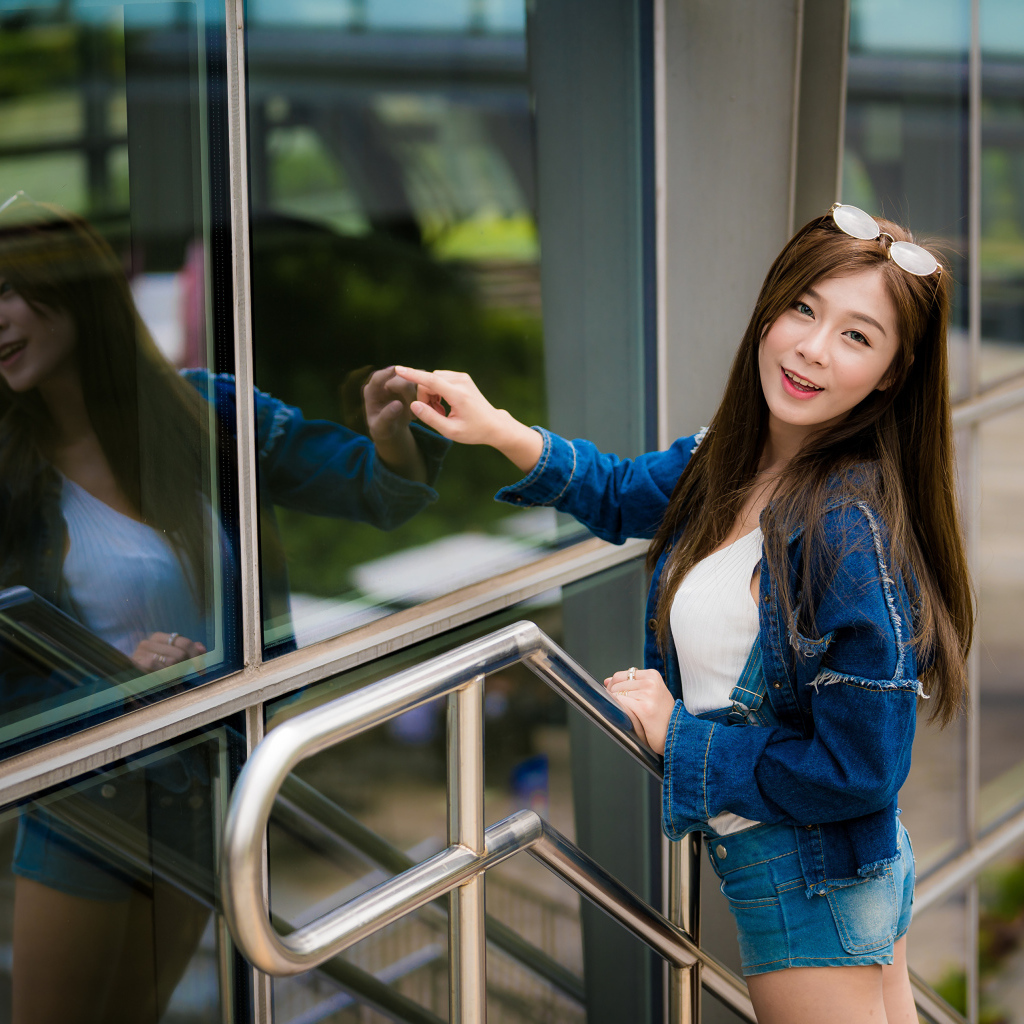 Улыбающаяся девушка в джинсовой куртке стоит у стены 