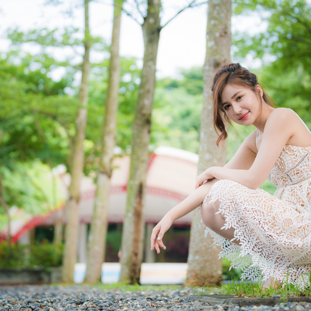 Улыбающаяся девушка в кружевном платье сидит под деревом в парке