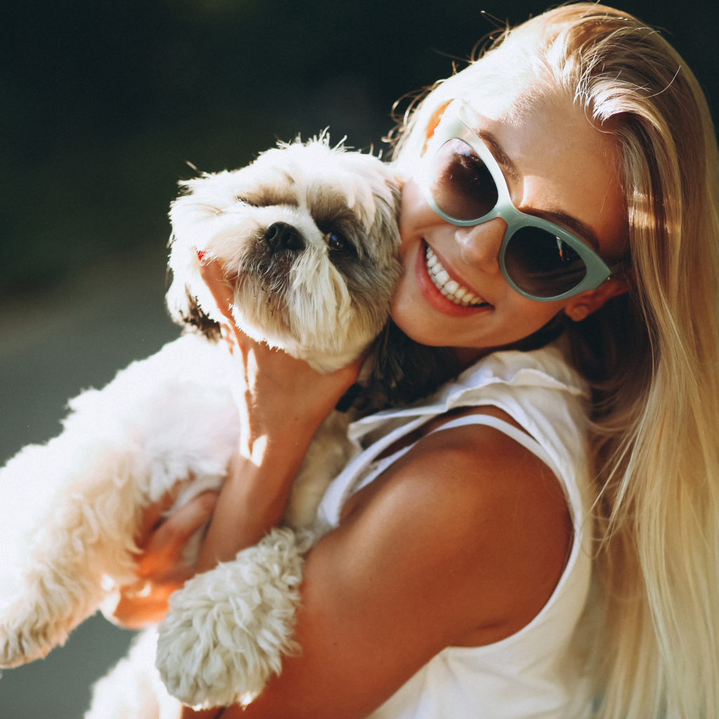 Улыбающаяся девушка в солнечных очках с собакой на руках