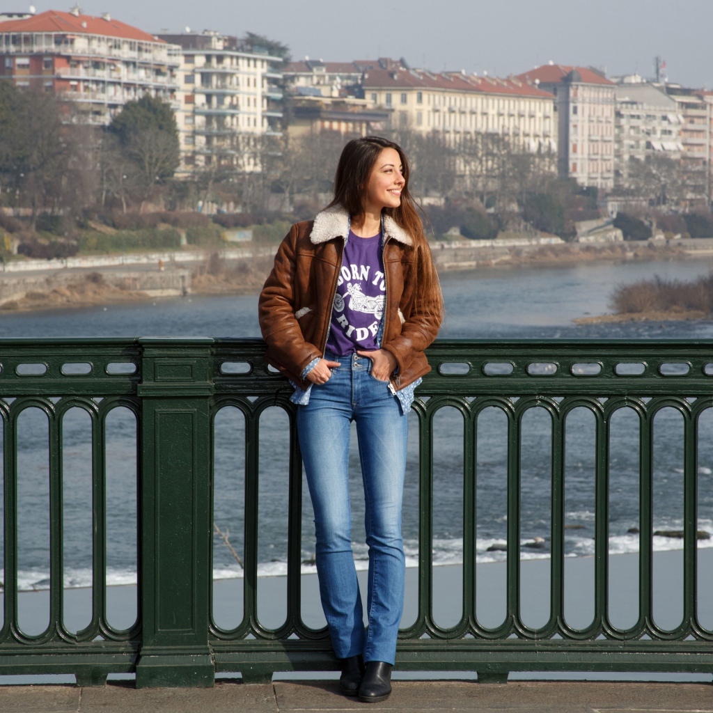 Улыбающаяся девушка стоит на мосту у реки