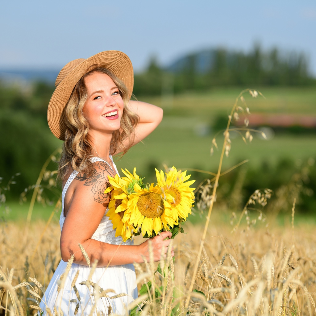 Улыбающаяся девушка с букетом подсолнухов на поле пшеницы