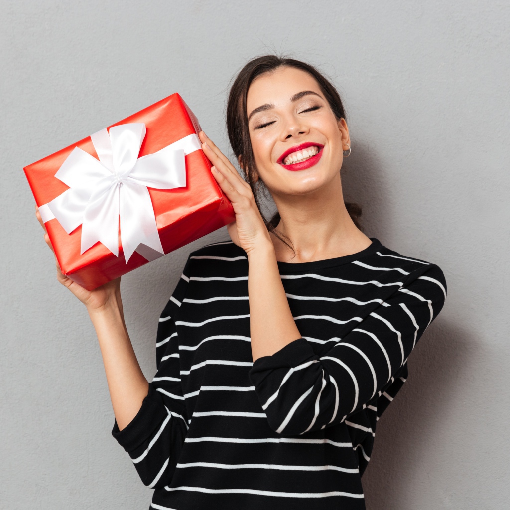 Улыбающаяся девушка с подарком в руках на сером фоне 