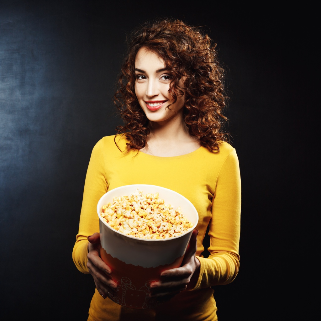 Улыбающаяся девушка с попкорном в руках на черном фоне 