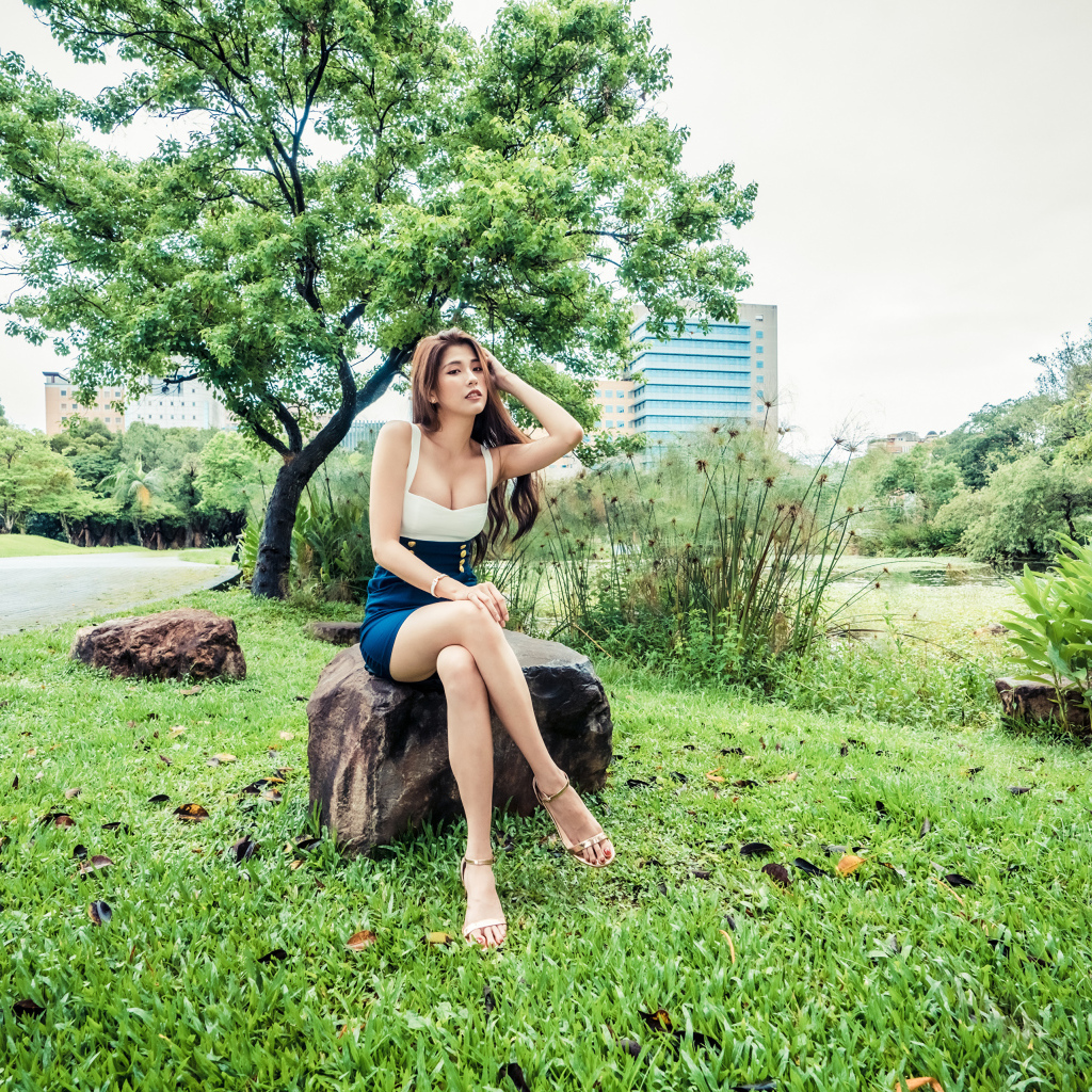 Эффектная девушка азиатка сидит на камне в парке