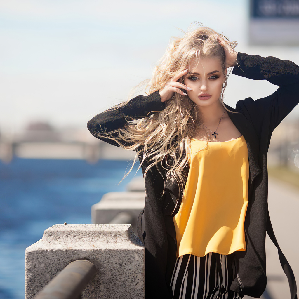 Эффектная блондинка в черном пальто стоит у воды