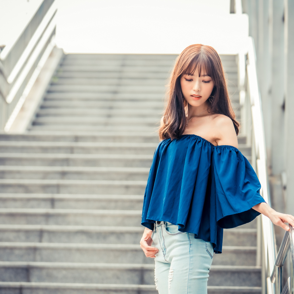 Стильная девушка азиатка с опущенной головой стоит на ступеньках 