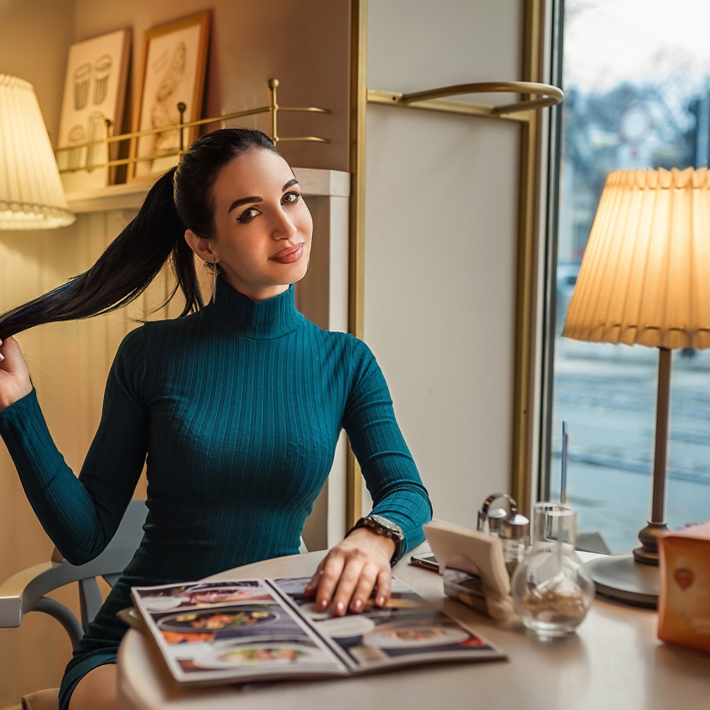 Стильная девушка в платье сидит в кафе у окна