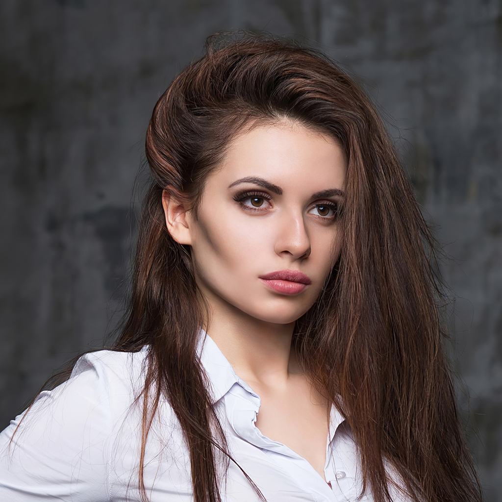 Стильная девушка в белой рубашке на фоне серой стены 