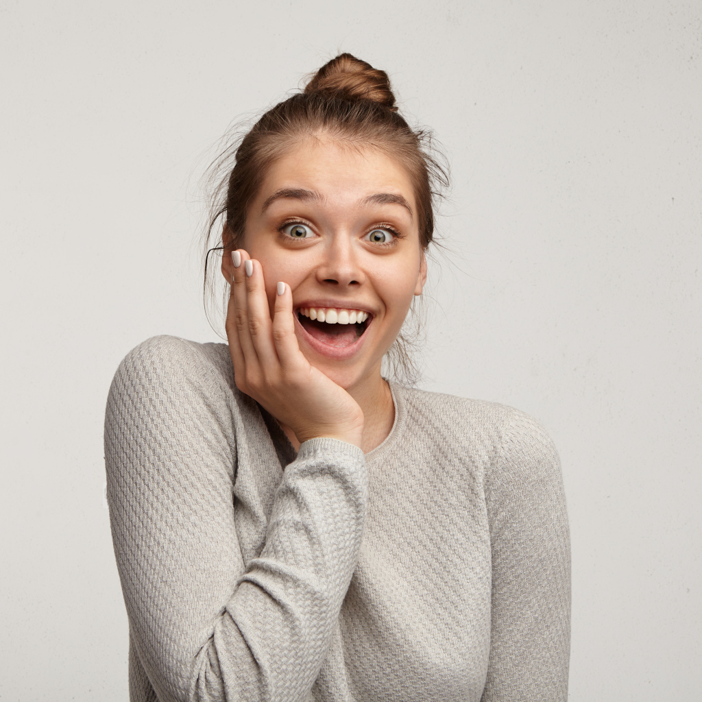 Удивленная девушка с рукой у лица на сером фоне 