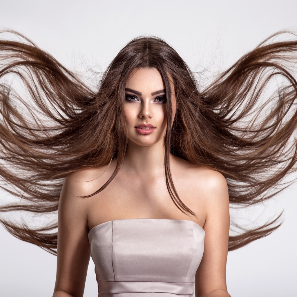 Ветер развивает волосы красивой девушке шатенке на сером фоне