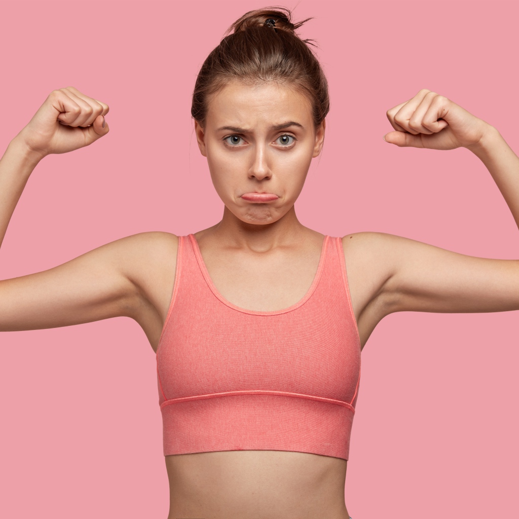 Расстроенная девушка без накаченных рук на розовом фоне