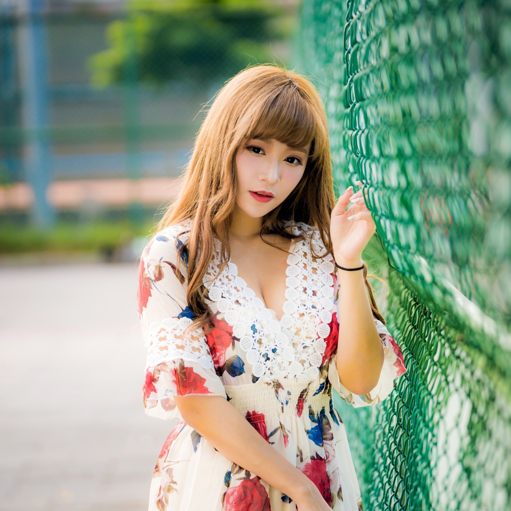 Молодая азиатка в платье у зеленой сетке 