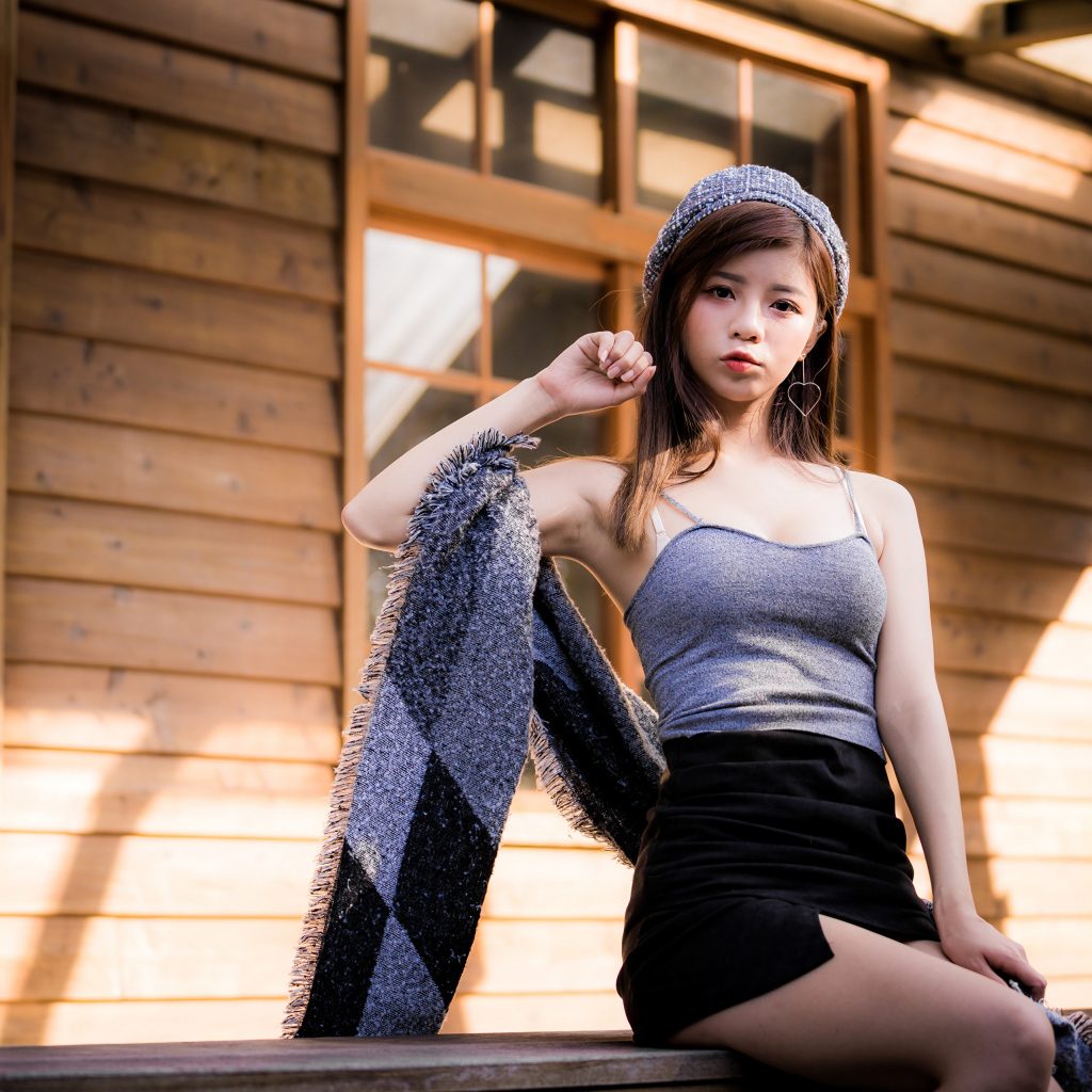 Молодая девушка азиатка в короткой юбке сидит на подоконнике 