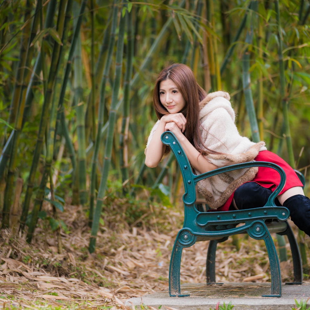 Молодая девушка азиатка сидит на зеленой лавке 
