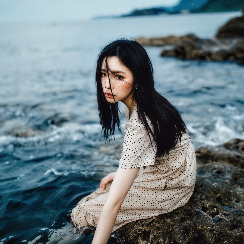 Молодая девушка азиатка сидит на камне у воды