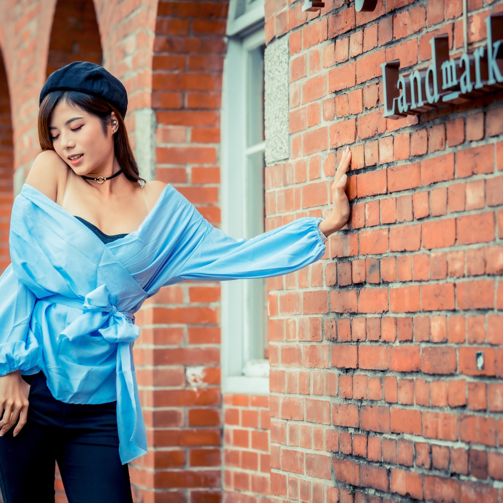 Молодая азиатка в черном берете стоит у стены 