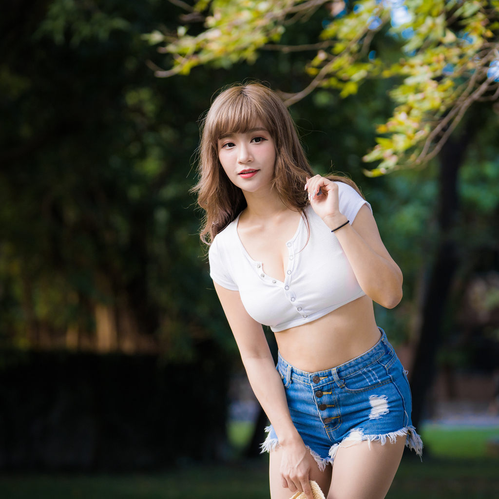 Молодая азиатка в белом топе и синих шортах  в парке