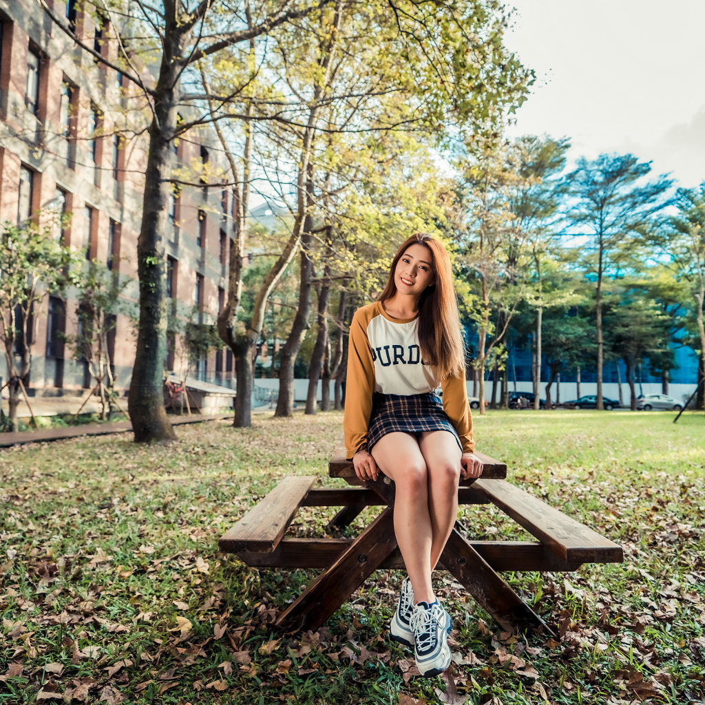 Молодая азиатка сидит на деревянном столе в парке 