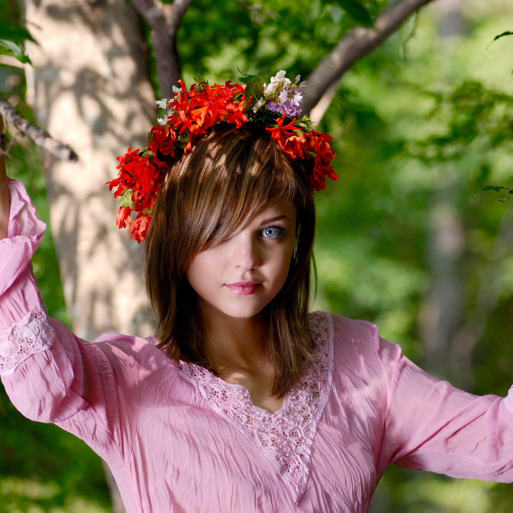 Молодая милая голубоглазая девушка с венком на голове у дерева