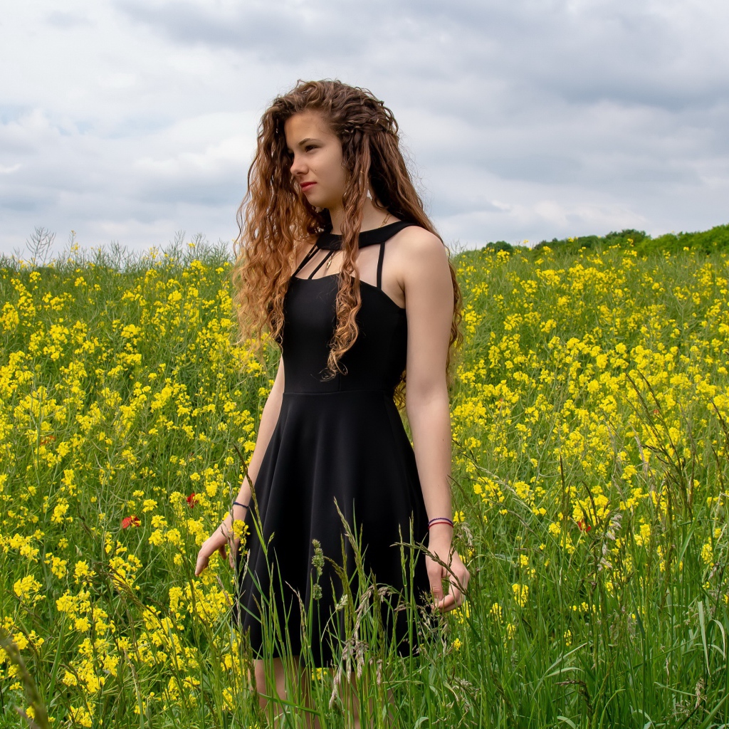 Молодая девушка в черном платье на поле с желтыми цветами