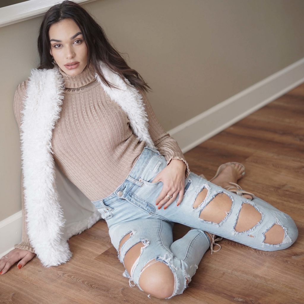 Молодая девушка в рваных джинсах сидит у стены