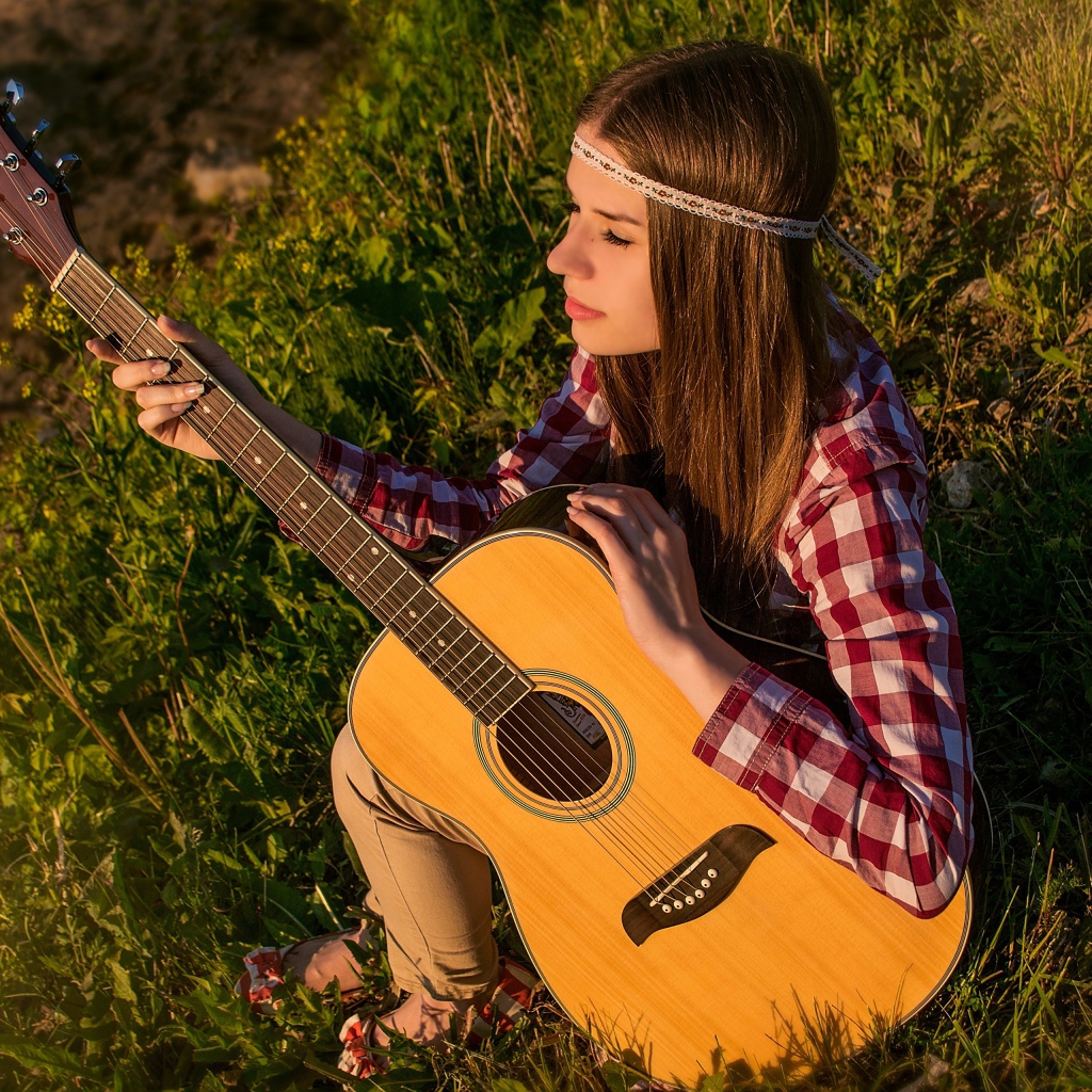 Молодая девушка хиппи сидит с гитарой на траве 