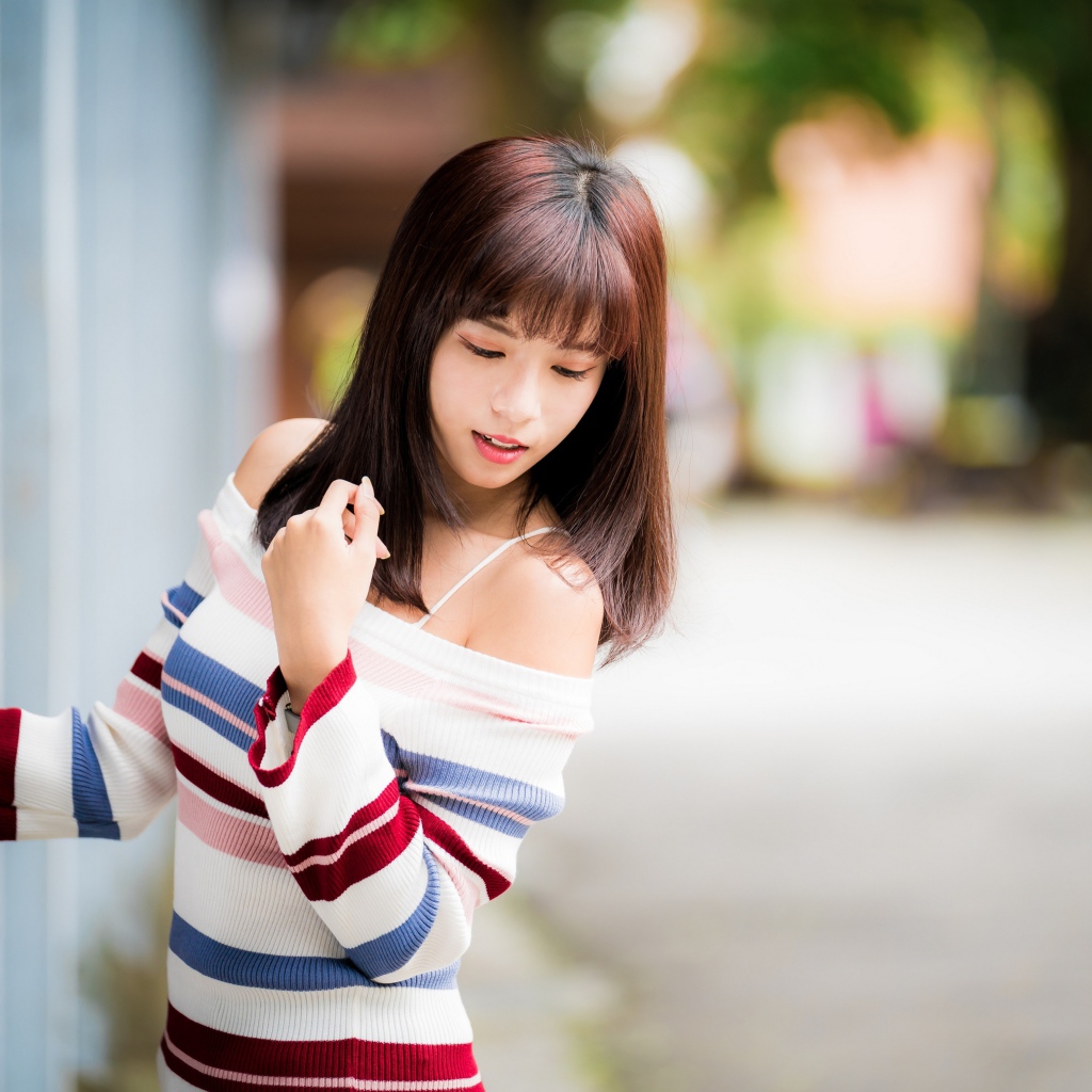 Молодая нежная девушка азиатка в свитере стоит у забора 