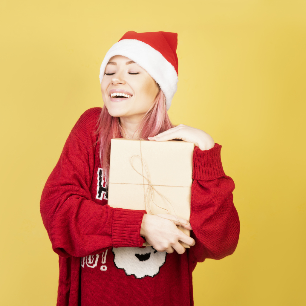 Улыбающаяся девушка в красном свитере с подарком на желтом фоне