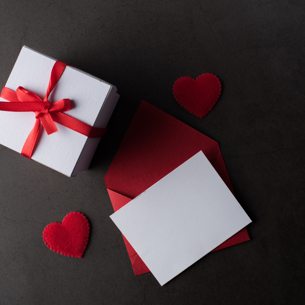 Конверт и подарок на сером столе с красными сердечками
