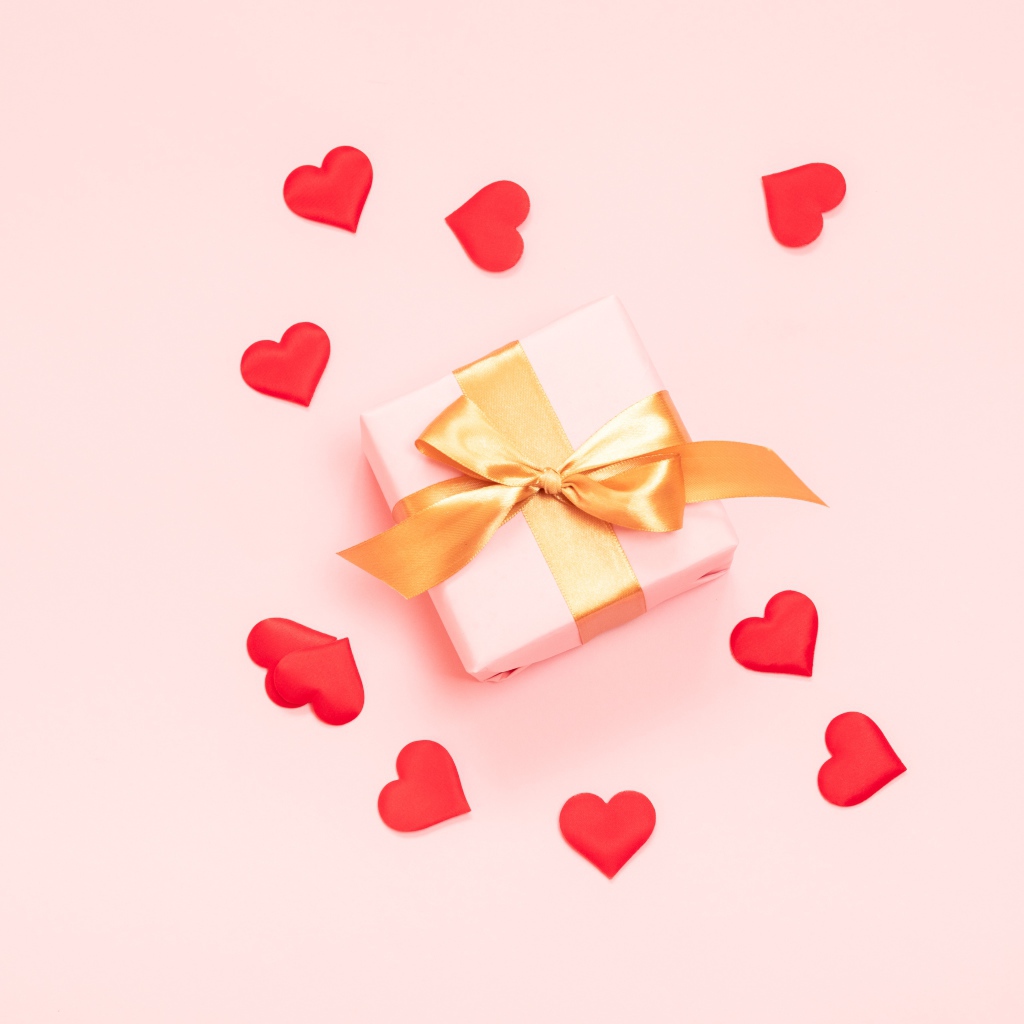 Gift with bow on a pink background with red hearts.