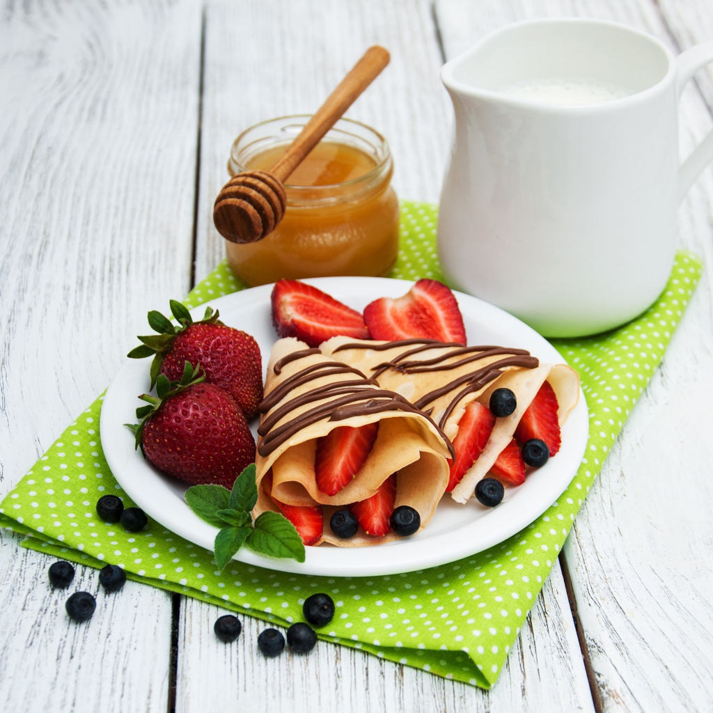 Delicious pancakes with strawberries on a table with milk and honey for Maslenitsa holiday