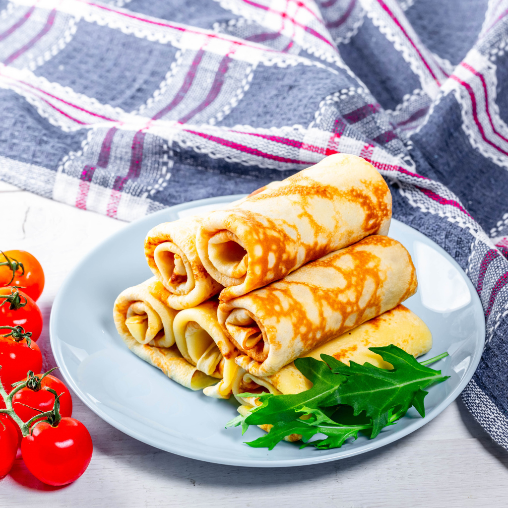 Блинчики на столе с помидорами и полотенцем угощение на Масленицу 2020