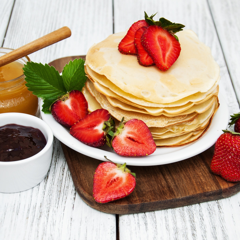 Блины с клубникой на столе с медом и джемом на праздник Масленица 2020