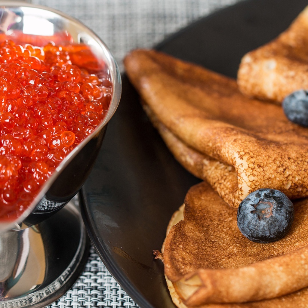 Тонкие блины с ягодами черники на столе с красной икрой на Масленицу