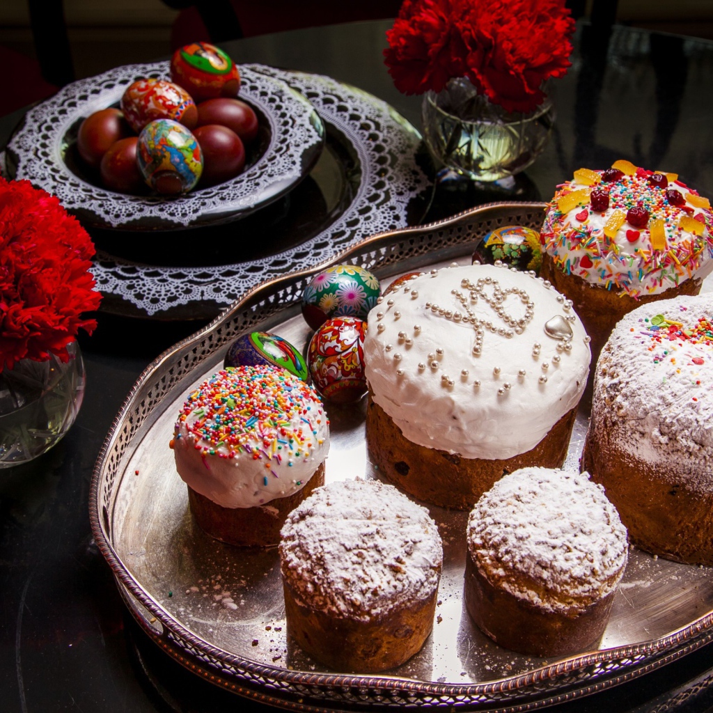 Много куличей на столе с гвоздиками и крашеными яйцами на праздник Пасха