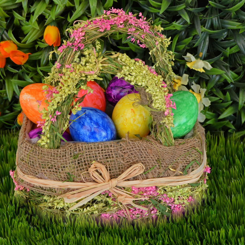 Разноцветные пасхальные яйца в корзине на зеленой траве на праздник 