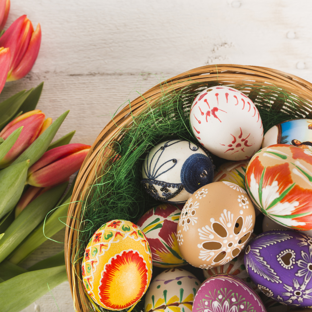 Разноцветные крашеные яйца в корзине с букетом тюльпанов на Пасху