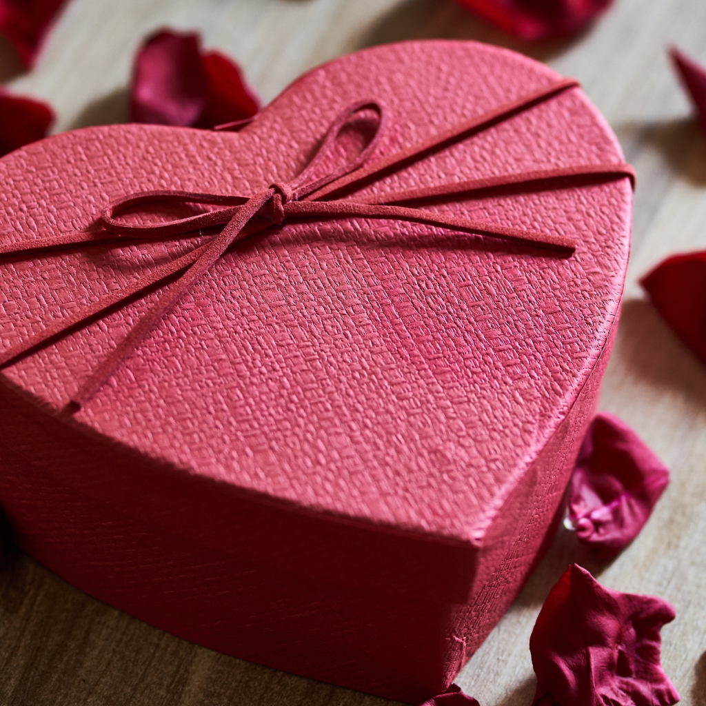 Большая красная коробка в форме сердца на столе с лепестками роз