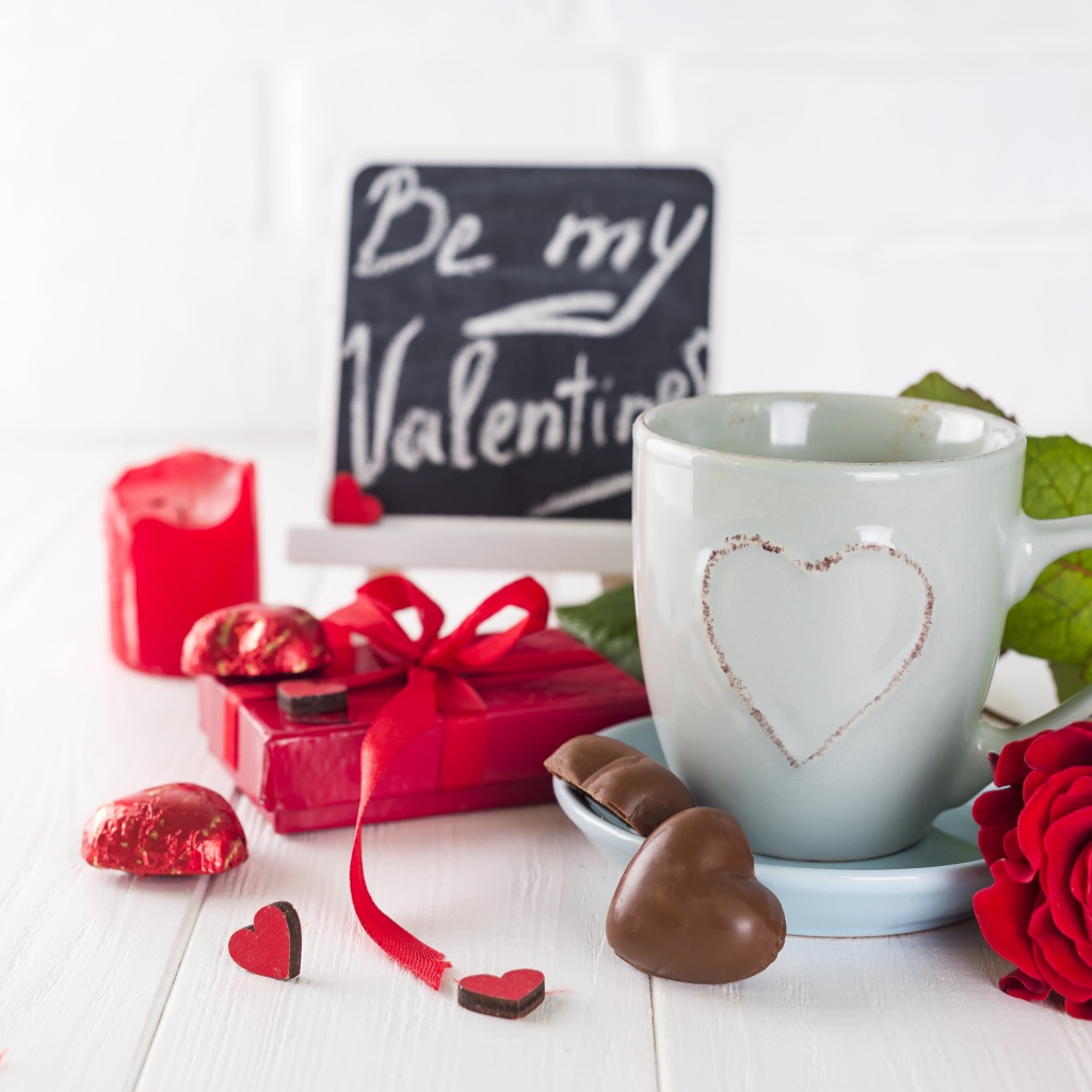 Белая чашка с конфетами и красной розой на столе в подарок на 14 февраля