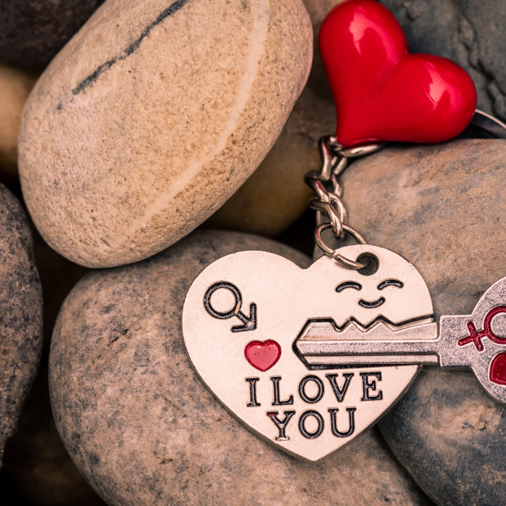 Брелок в форме сердца с ключом лежит на камнях 