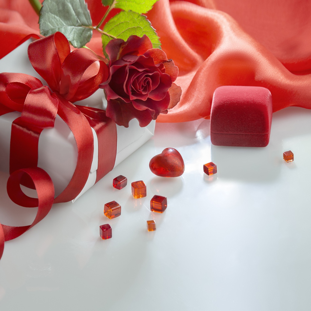 Подарки на белом столе с розой и красной тканью