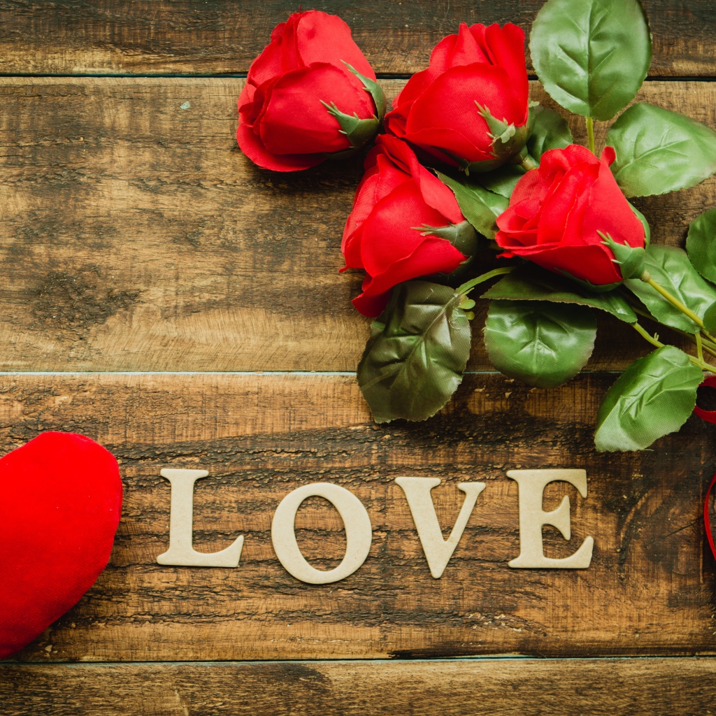 Надпись LOVE на столе с розами и красным сердцем
