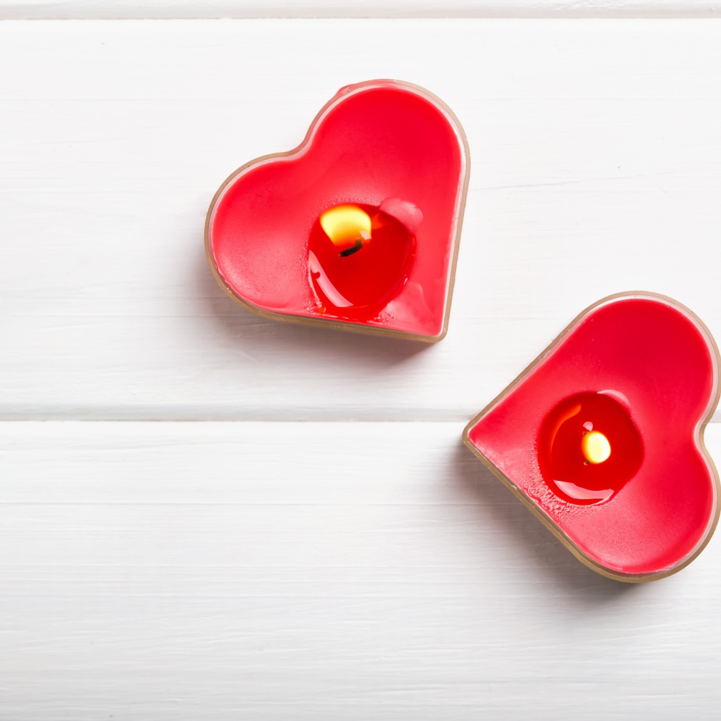 Две зажженные свечи в форме сердца на столе 