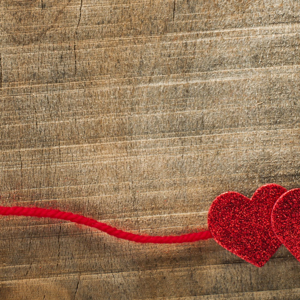 Два красных сердца со шнурком на деревянном фоне