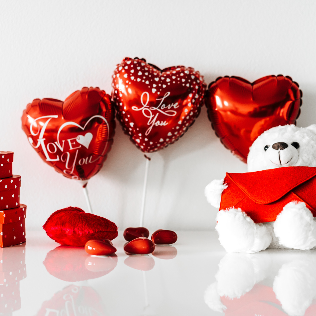 Белый мишка с подарками и шариками у стены